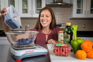 Dr. Claire Berryman in a nutrition lab dumping blue berries from a plastic container onto a food scale