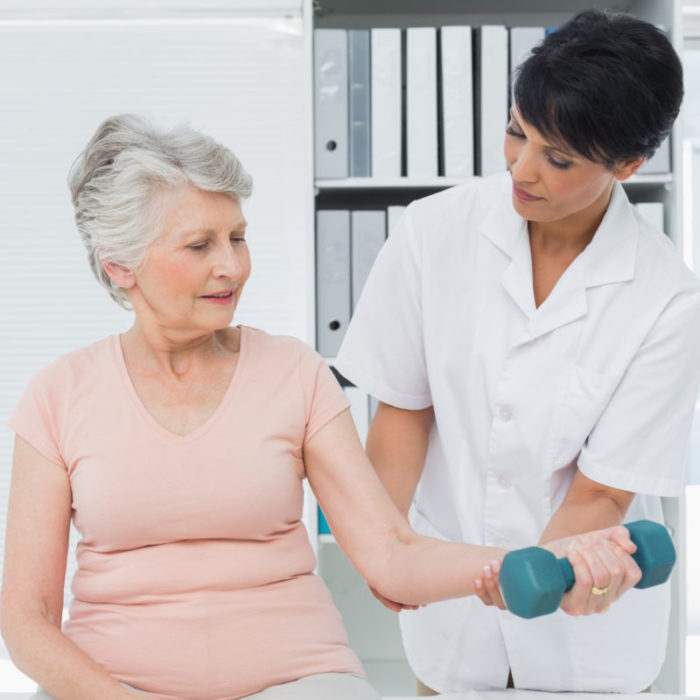 Female physiotherapist assisting senior woman to lift dumbbell in the medical office